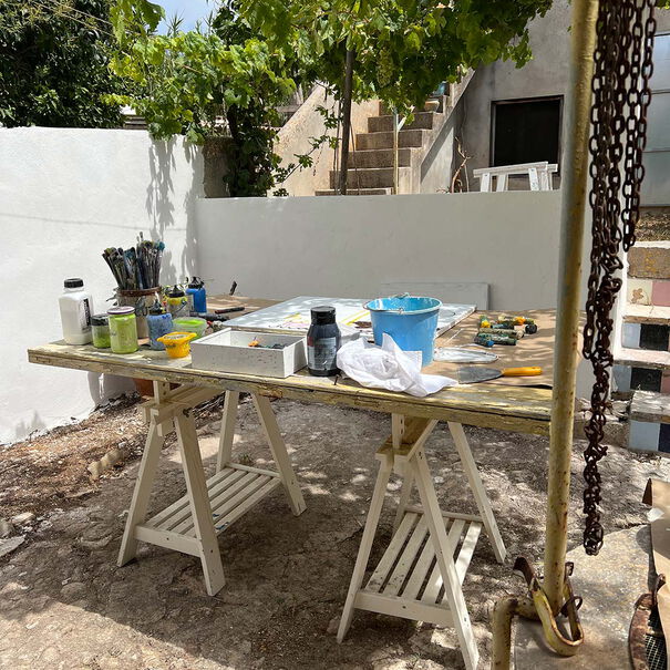 Paints, brushes and canvas are on a jacked-up wooden board outside with other tools.